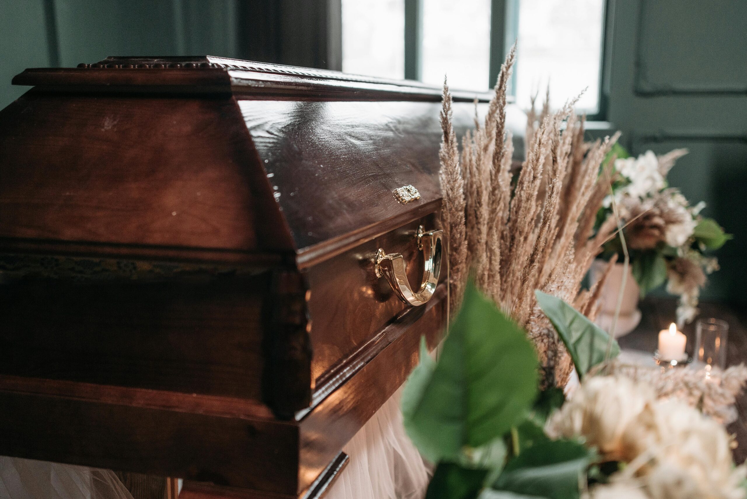A beautiful funeral display featuring a wooden coffin with flowers and candles indoors.